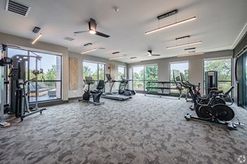 A spacious gym with a variety of exercise equipment and large windows.